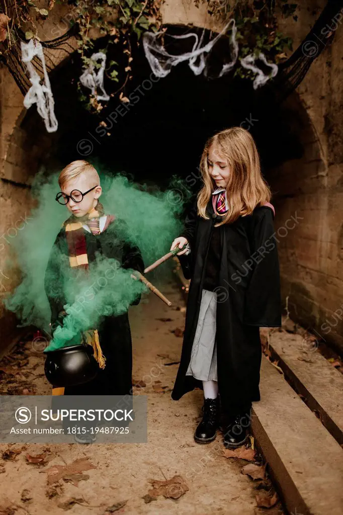 Smiling girl with brother holding magic cauldron standing in front of tunnel