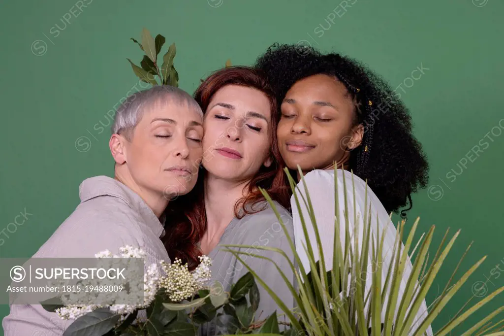 Multiracial friends with eyes closed standing against green background