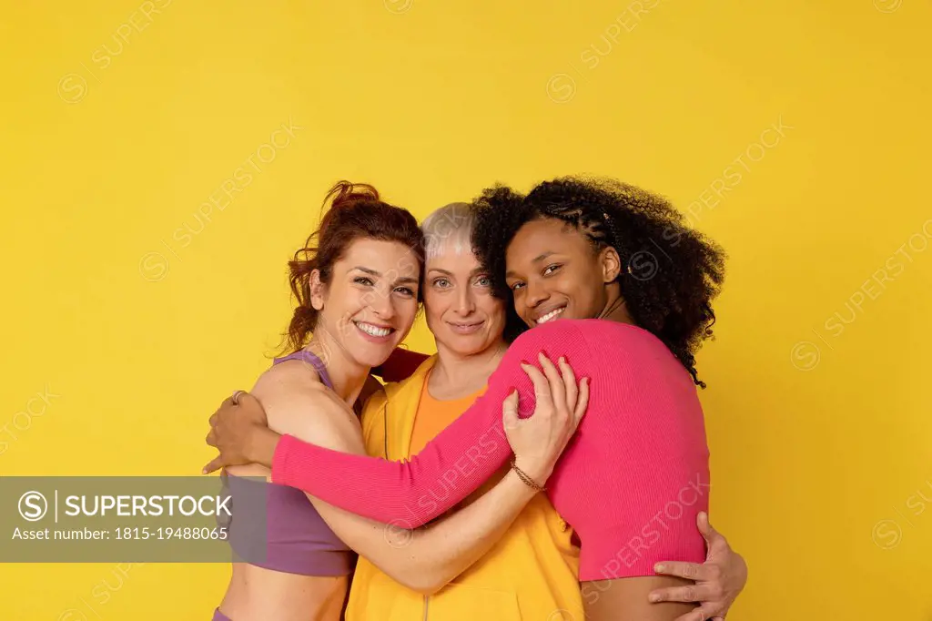 Smiling multiracial friends hugging each other against yellow background