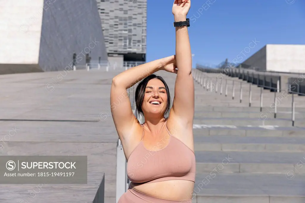 Smiling curvy woman wearing sports clothing standing with eyes closed on stairs