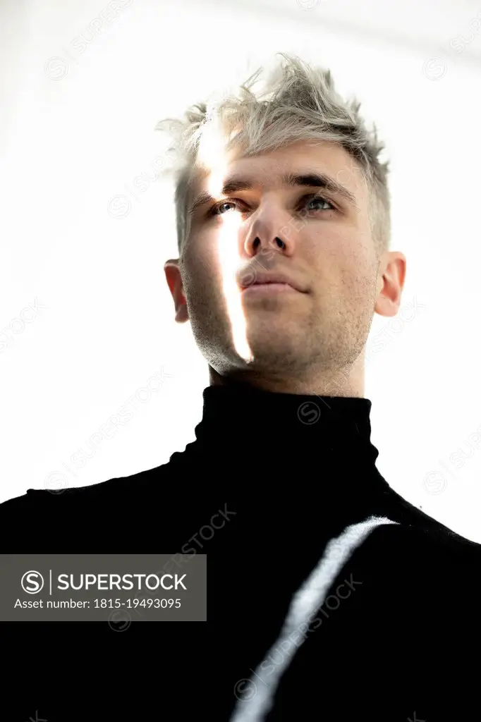 Young man with beam of light on face against white background