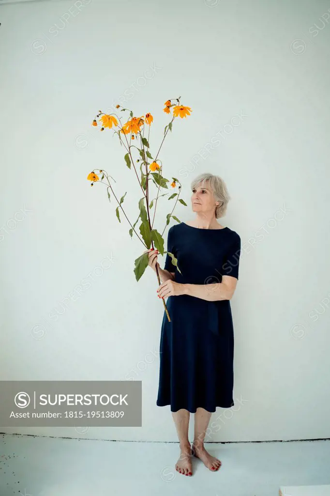 Senior senior woman with twig standing in front of wall