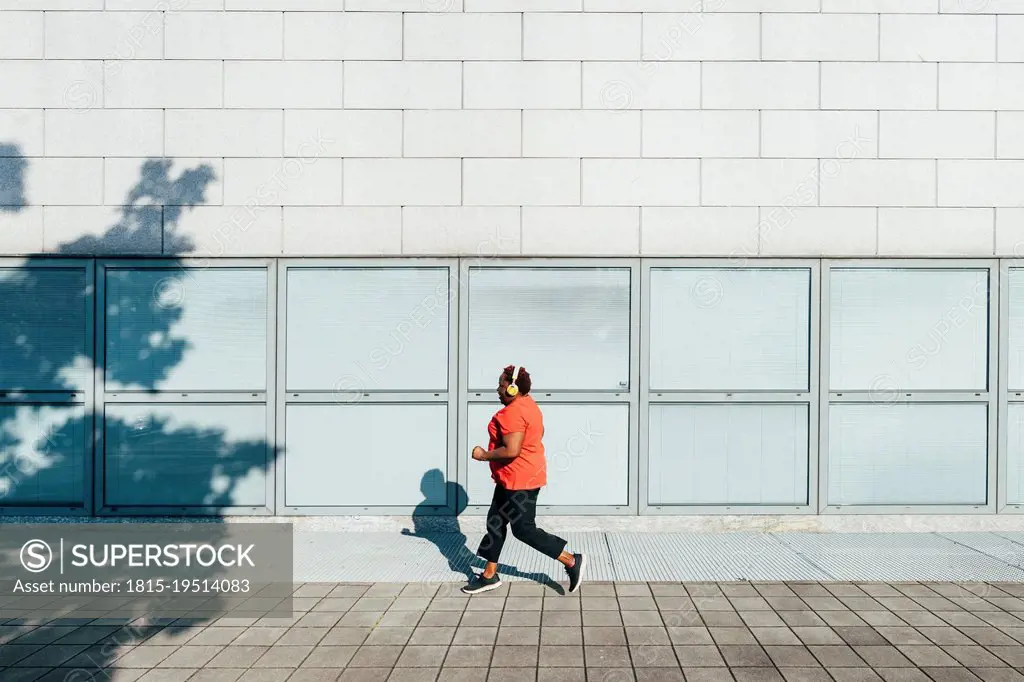 Woman listening music through wireless headphones jogging on footpath