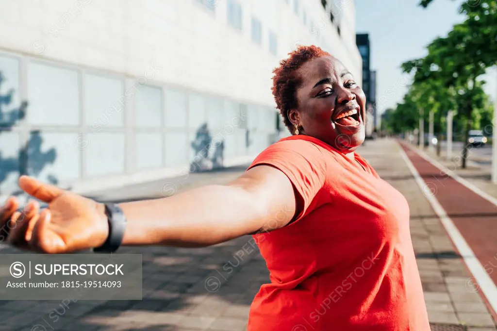 Cheerful woman standing with arms outstretched on sunny day