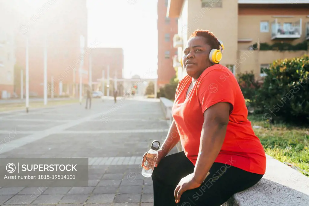 Woman sitting with water bottle listening music through wireless headphones