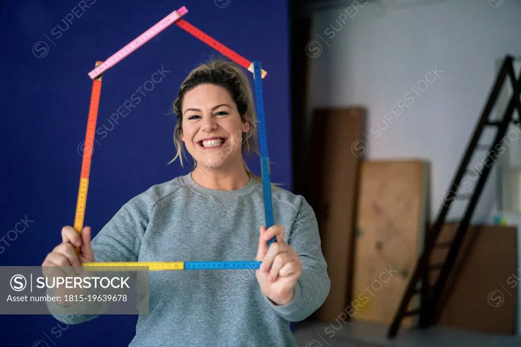 Smiling woman holding ruler house model at home