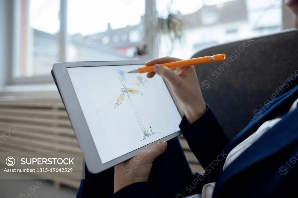 Hand of businesswoman drawing wind turbine on tablet PC in office