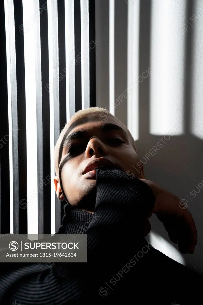 Man wearing turtleneck top leaning on wall