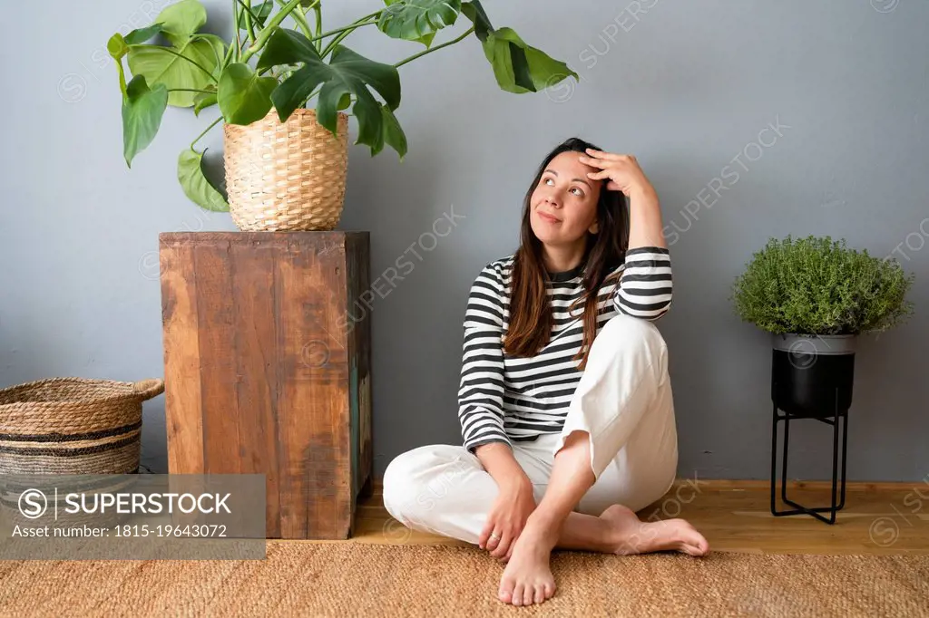 Contemplative woman with head in hands sitting on floor at home