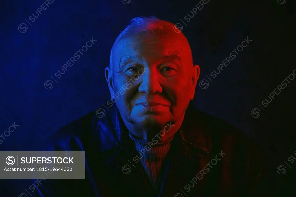 Senior man's face illuminated with red and blue neon light against black background