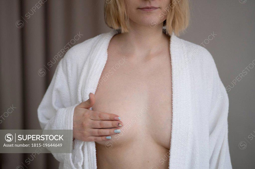 Young woman wearing bathrobe covering breast with hand - SuperStock