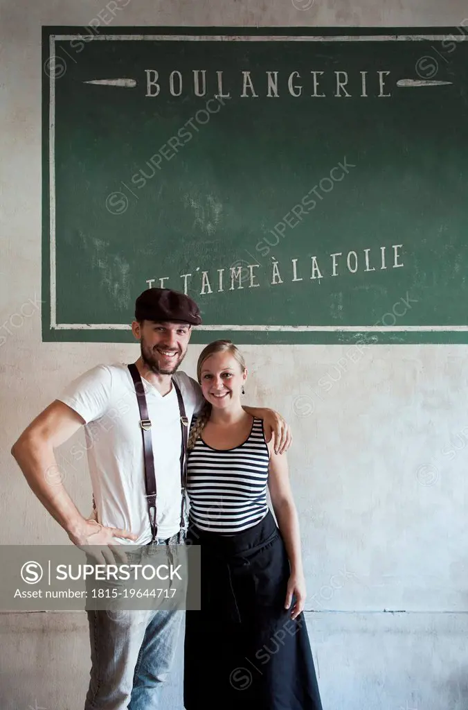 Baker with arm around coworker standing in front of wall with French text