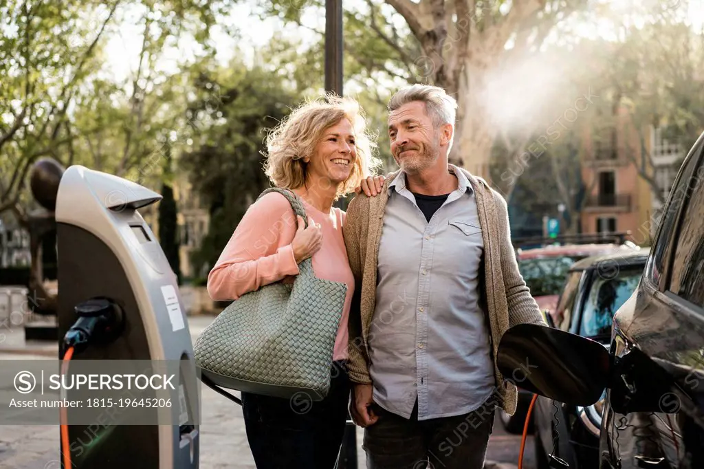 Smiling mature couple charging electric car