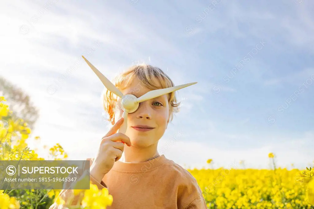 Boy playing with wind turbine model at rapeseed field