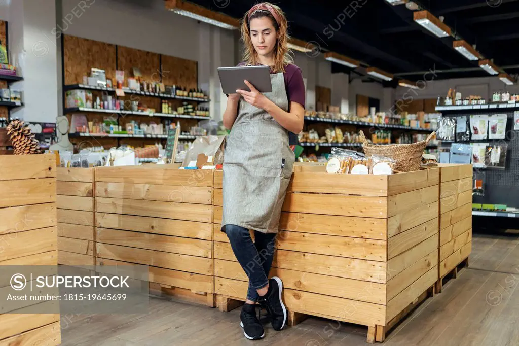 Store owner using tablet PC leaning on crate at organic market