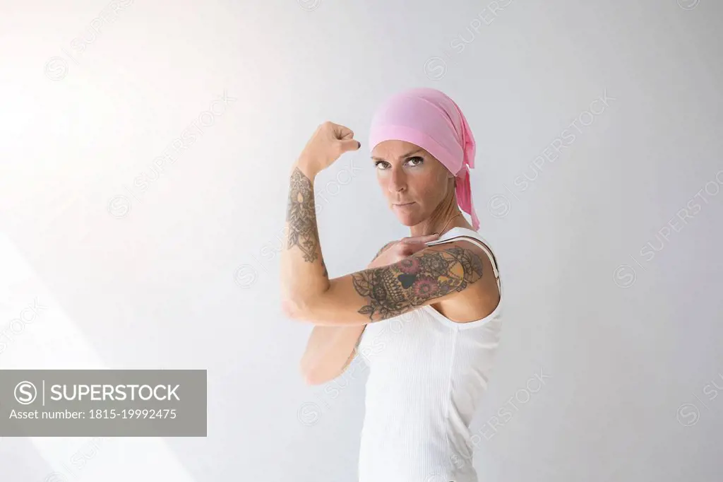 Woman wearing pink scarf flexing muscles in front of wall