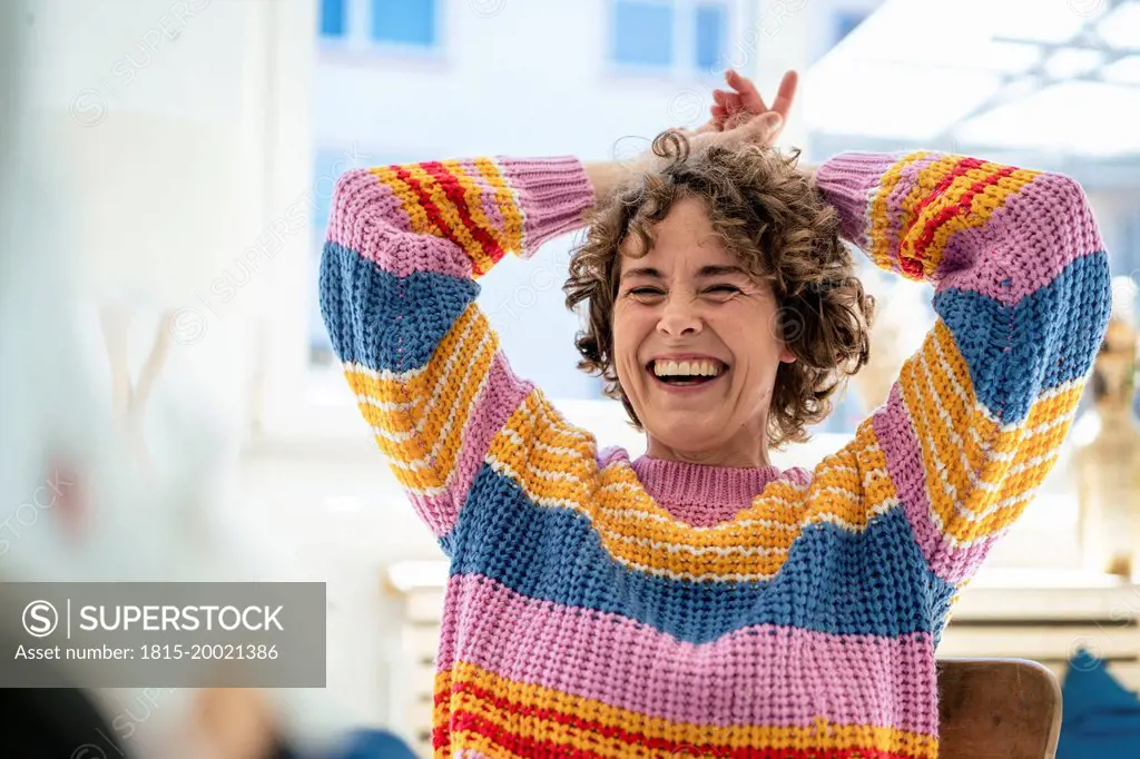 Happy woman sitting with hands behind head at home