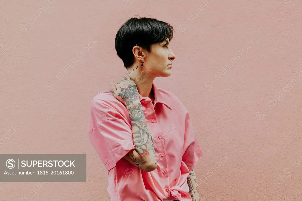 Thoughtful woman with short hair standing in front of peach wall