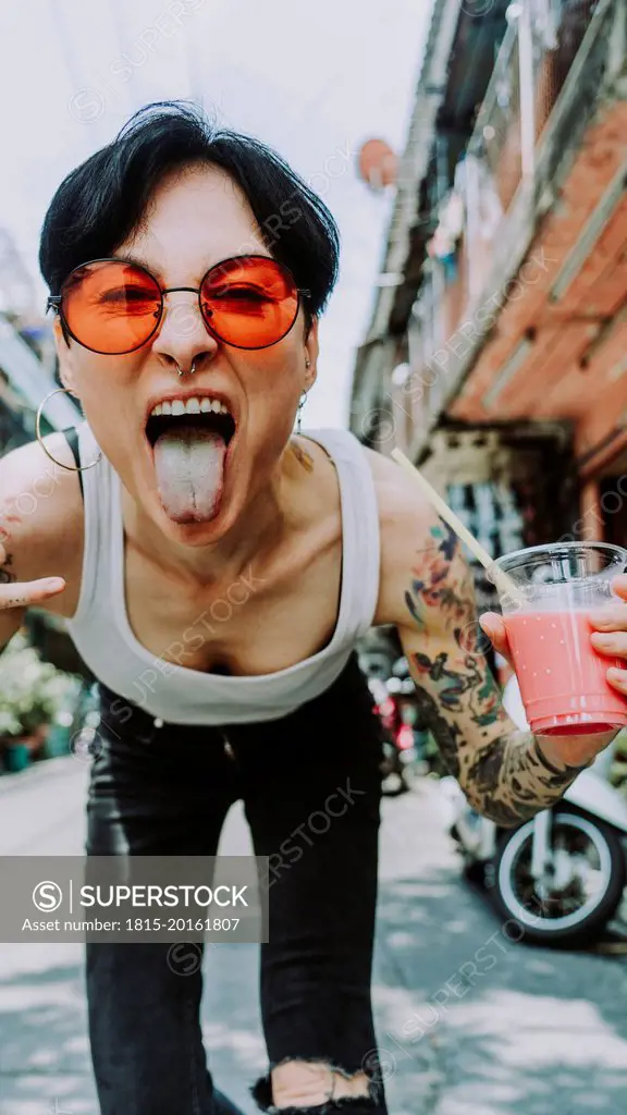 Tattooed woman sticking out tongue holding glass of drink