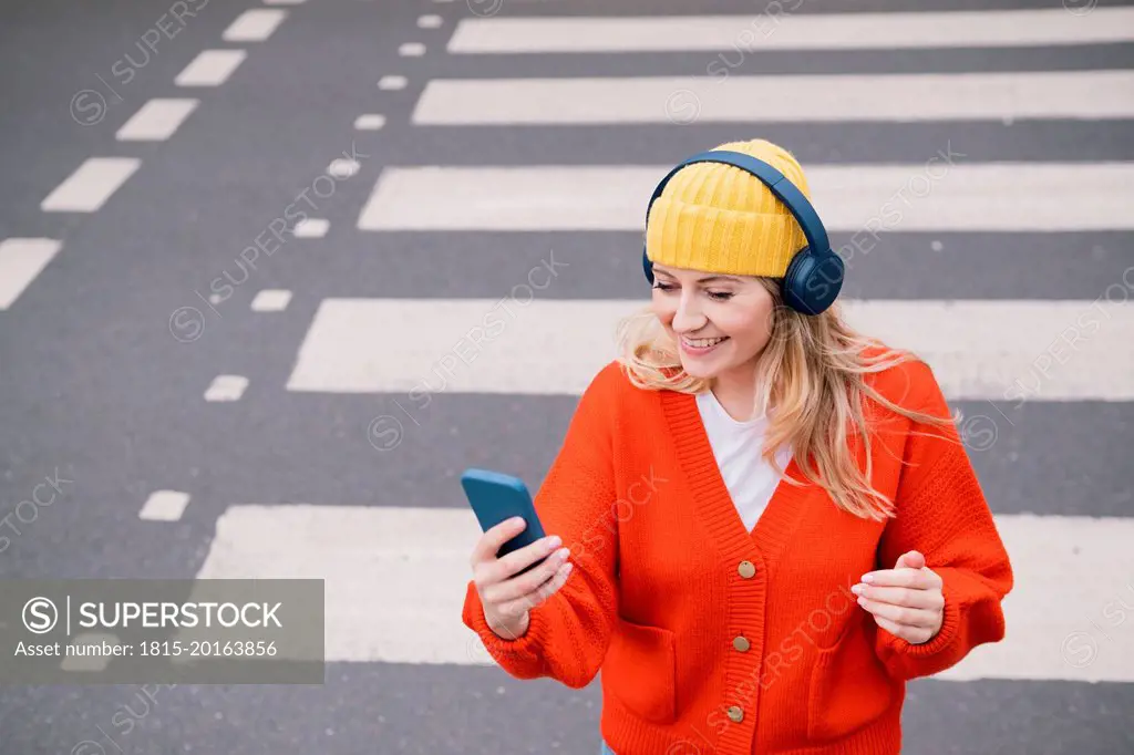 Smiling woman wearing wireless headphones crossing road