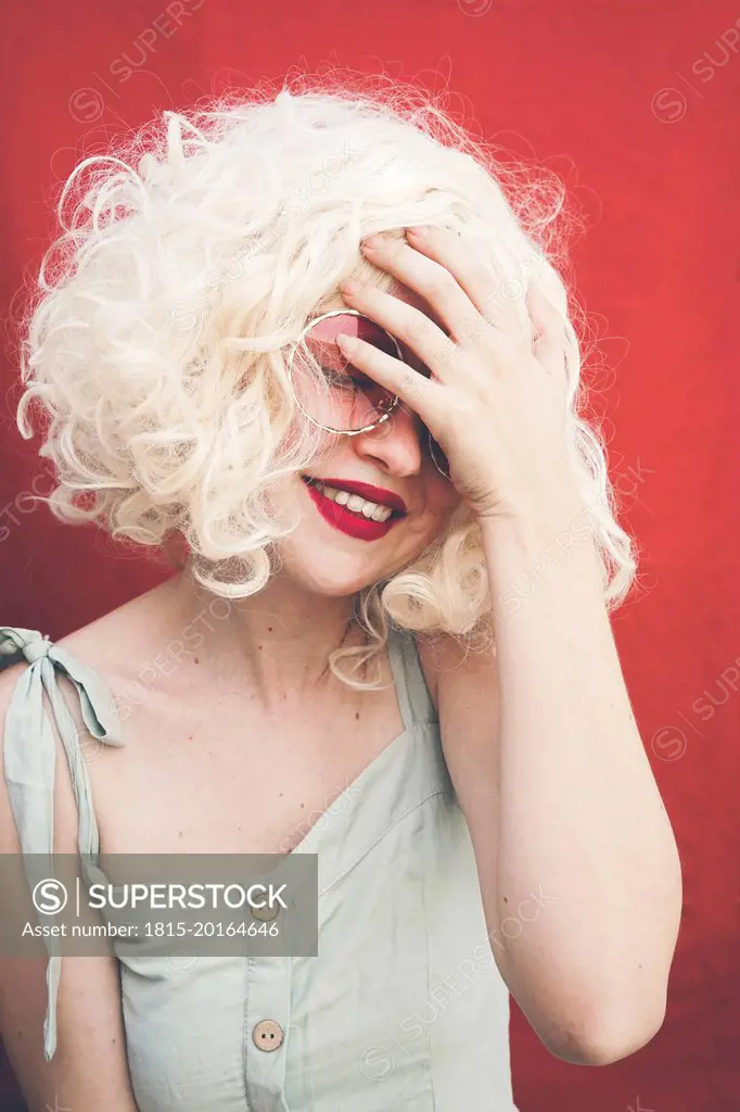 Smiling blond woman touching forehead against red background