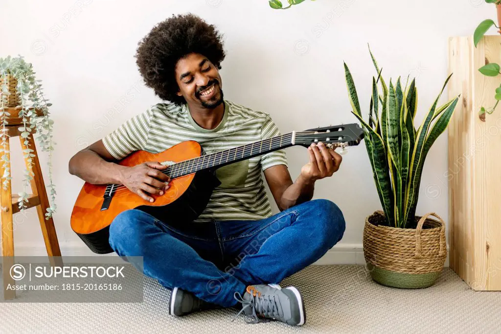 Happy African man playing guitar in front of wall at home