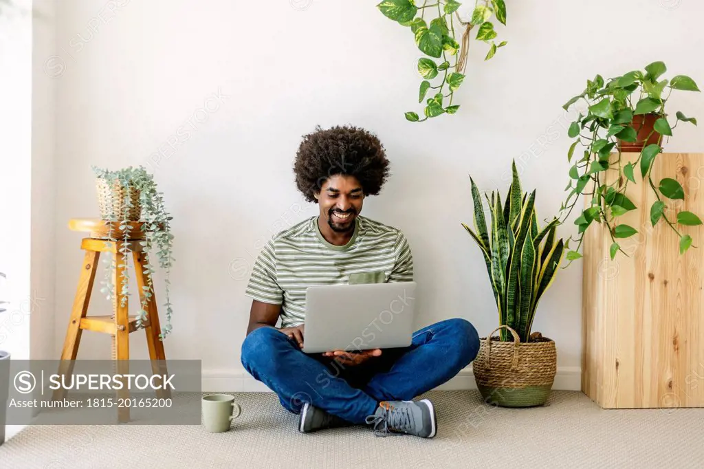 Happy man using laptop sitting in front of wall at home