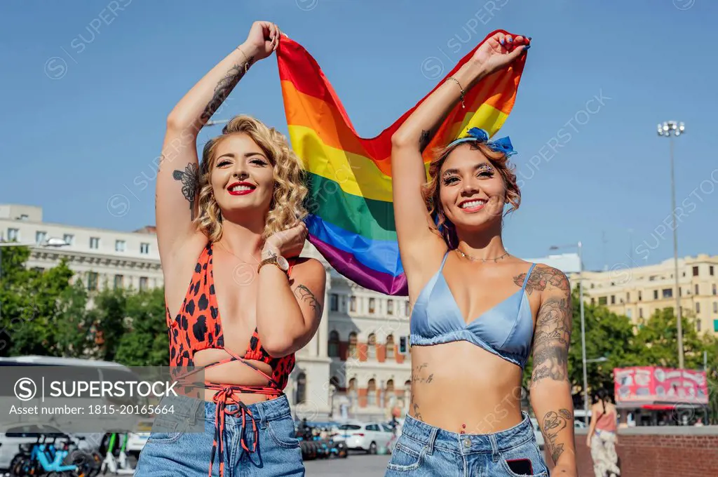 Happy women holding rainbow flag on sunny day
