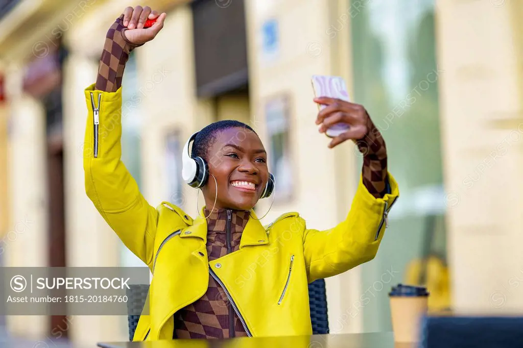 Cheerful woman with hand raised taking selfie through smart phone