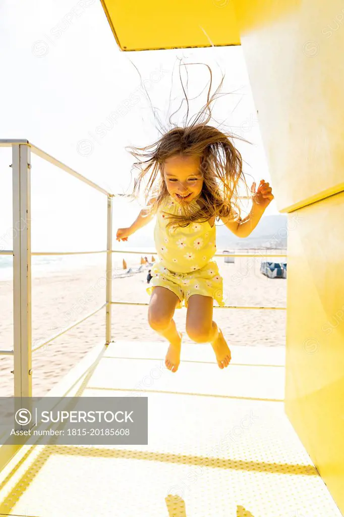 Cheerful girl jumping on yellow lifeguard hut