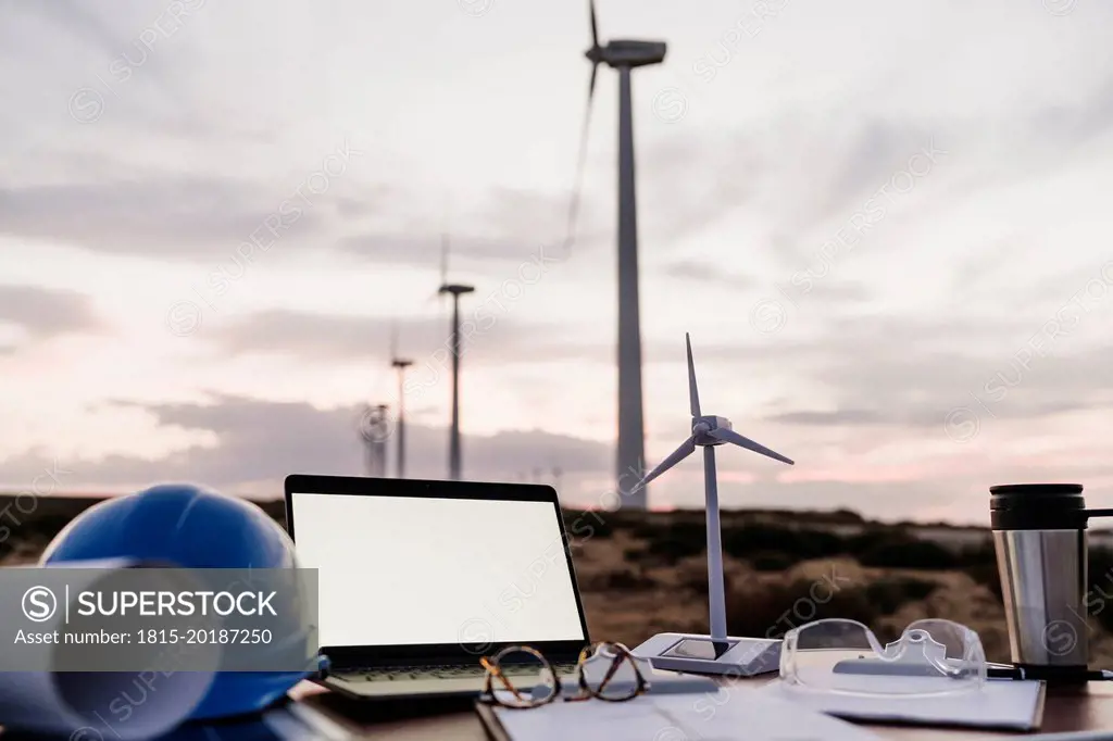 Wind turbine model by laptop with blank screen on desk at wind farm