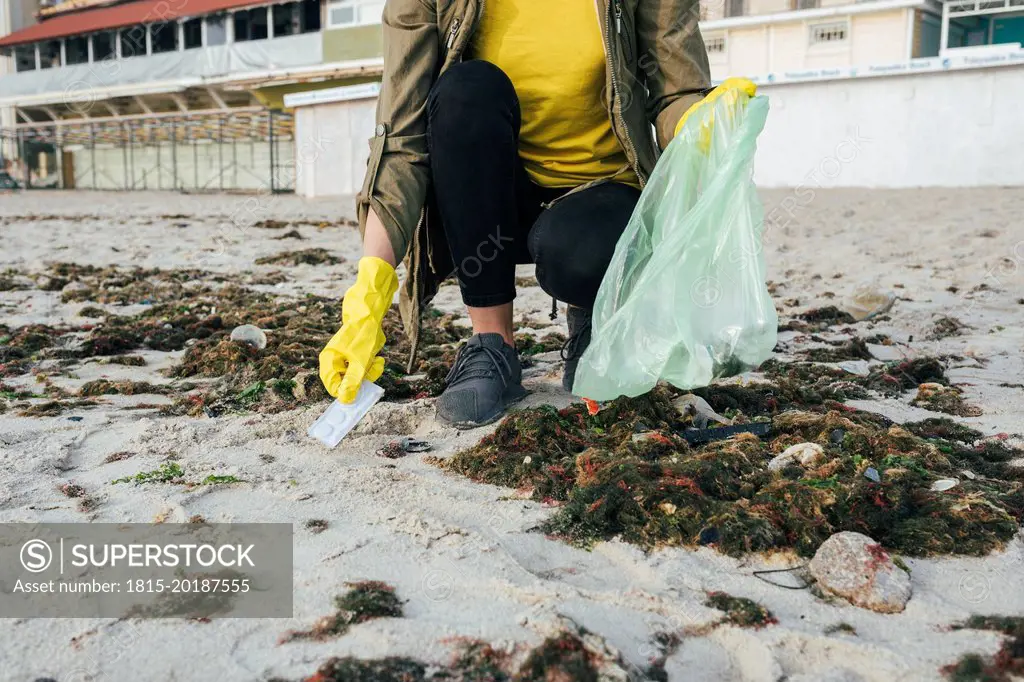 Volunteer crouching and picking up trash from beach