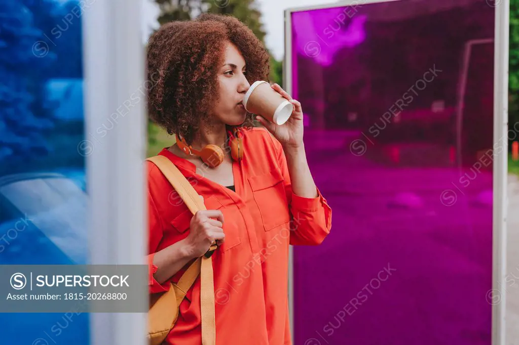 Young woman drinking coffee near magenta and blue glasses