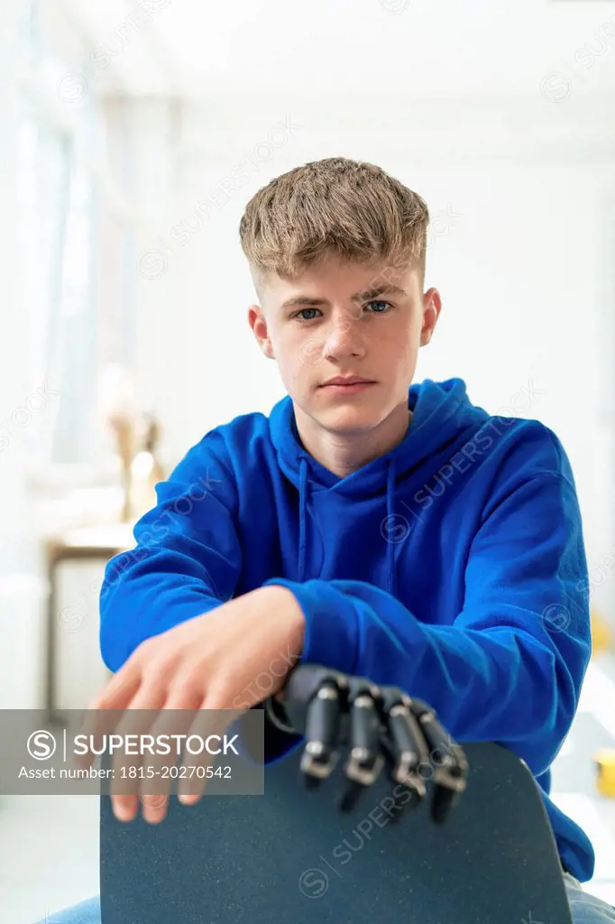 Confident teenage boy with amputated arm sitting on chair