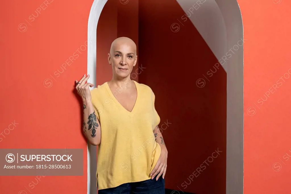 Confident bald woman with hand on hip at doorway