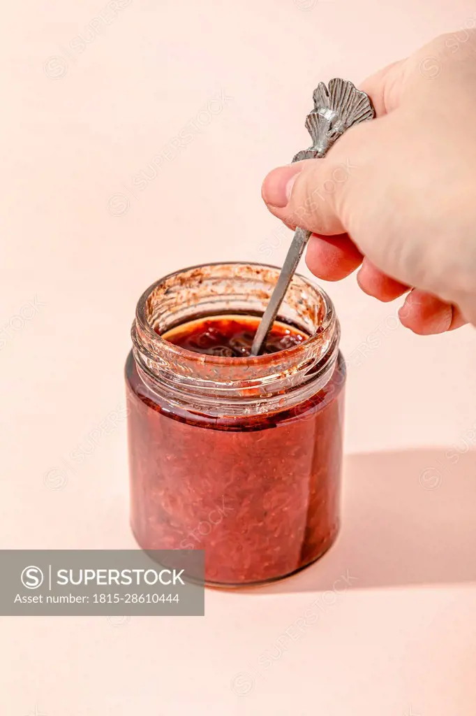 Hand of woman holding spoon with homemade strawberry jam over peach background