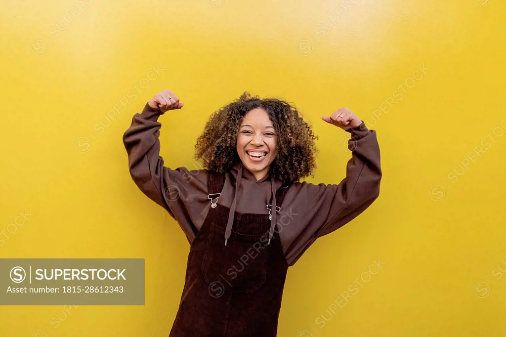 Happy woman flexing muscles in front of yellow wall