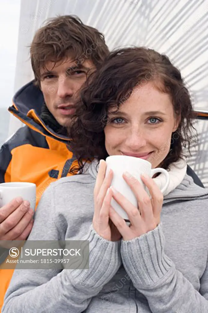Germany, Baltic Sea, Lübecker Bucht, Young couple on sailing boat sitting and holding mugs, portrait