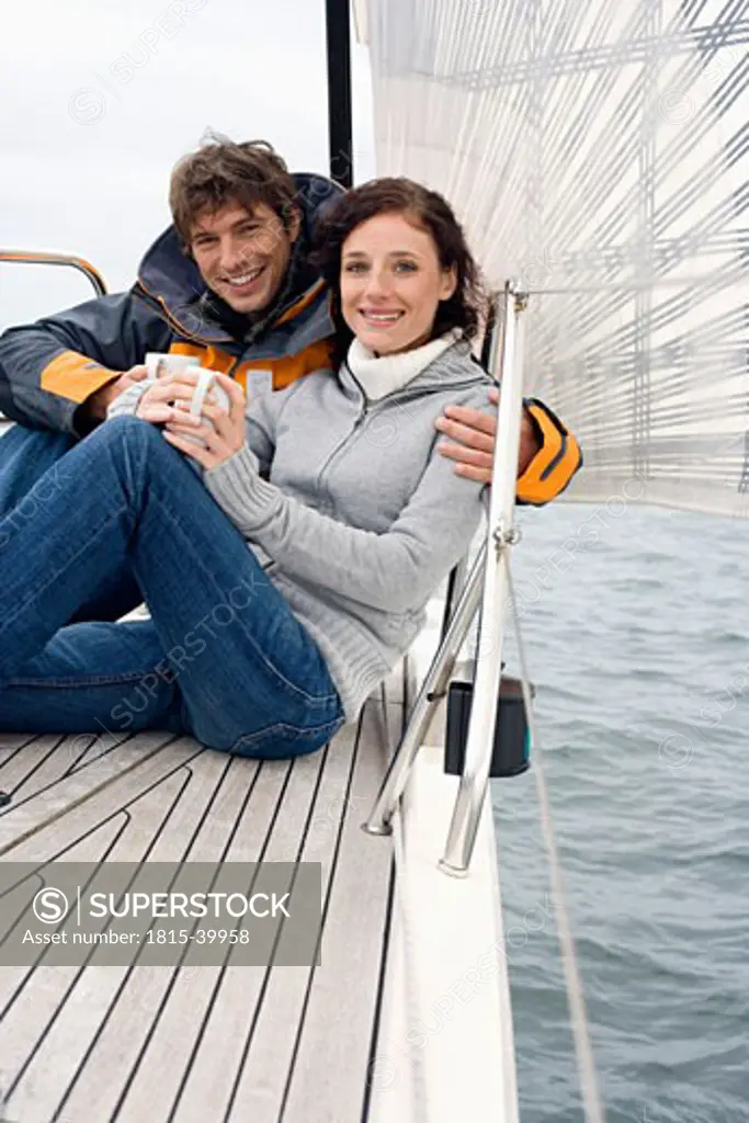 Germany, Baltic Sea, Lübecker Bucht, Young couple on sailing boat sitting and holding mugs