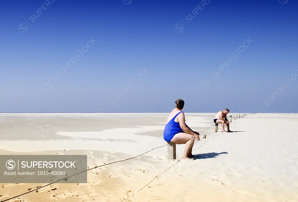 Man and woman sitting on post of fence at beach