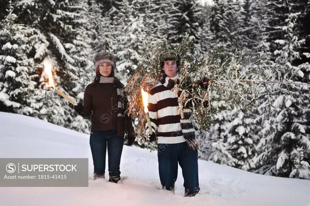 Austria, Salzburger Land, Altenmarkt, Young couple with fir tree and torches in the snow