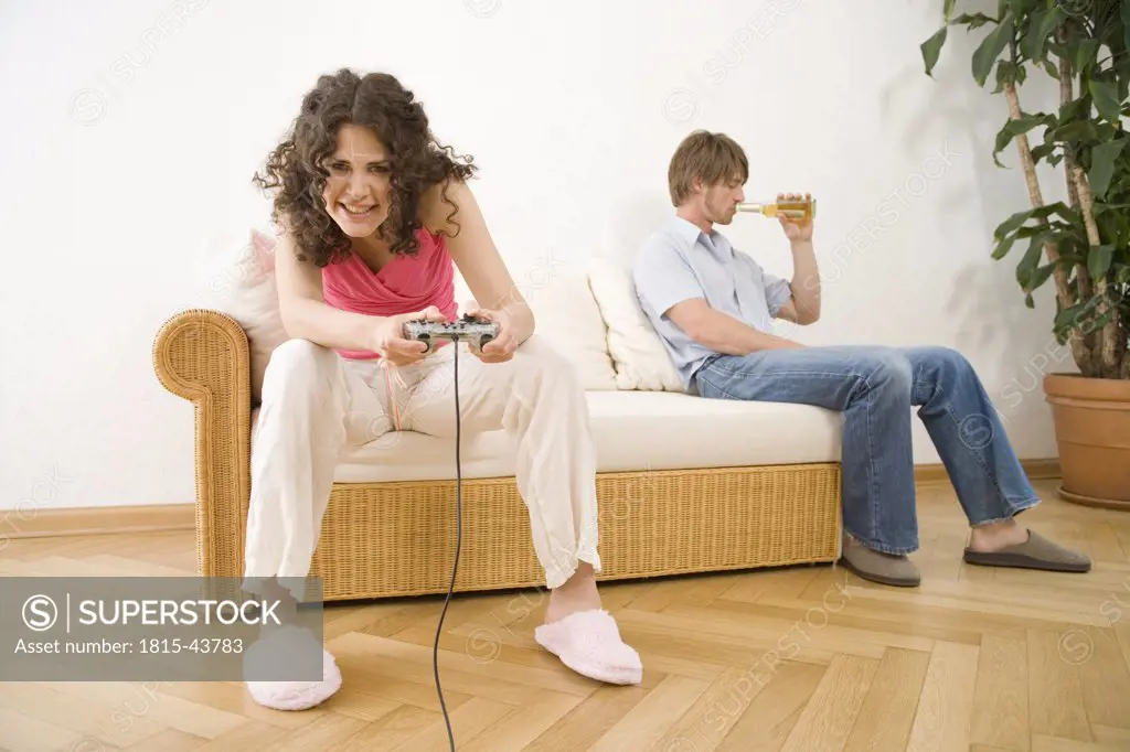 oung woman playing game with hand held controls, by man sitting on sofa