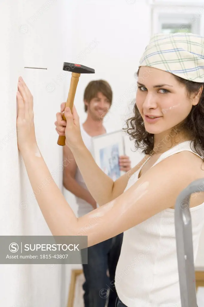 Young woman hammering picture hook on wall, side view