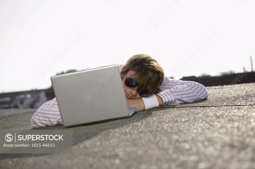 Man with laptop, wearing sun glasses, lying on belly, portrait