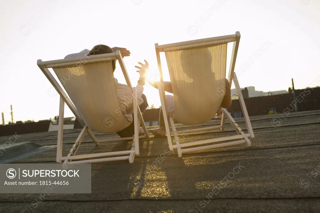 Couple sitting in deck chairs on roof, watching sun set
