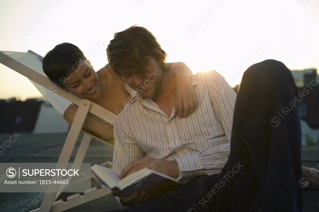Young couple, woman sitting in deck chair, man reading book