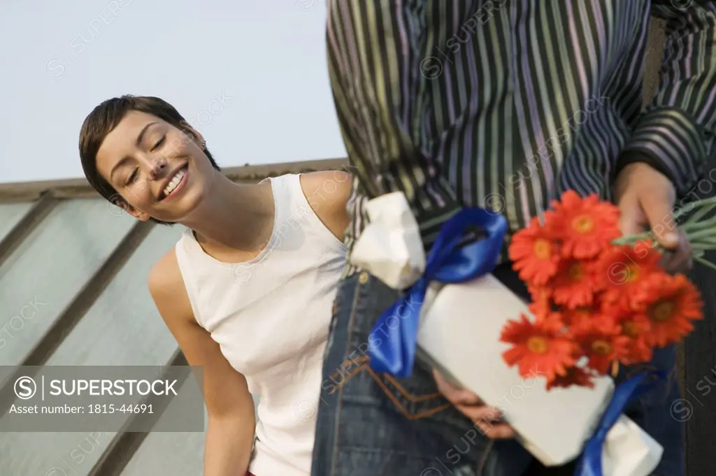 Young couple, man hiding present and flowers behind back