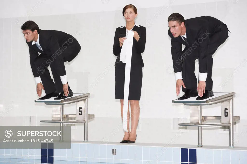 Businessmen crouching on starting blocks, woman holding roll of paper