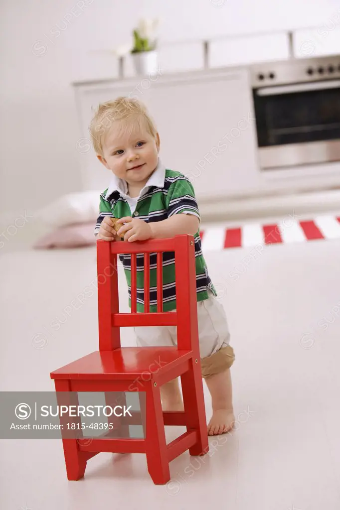 Baby boy (1-2) standing behind red chair
