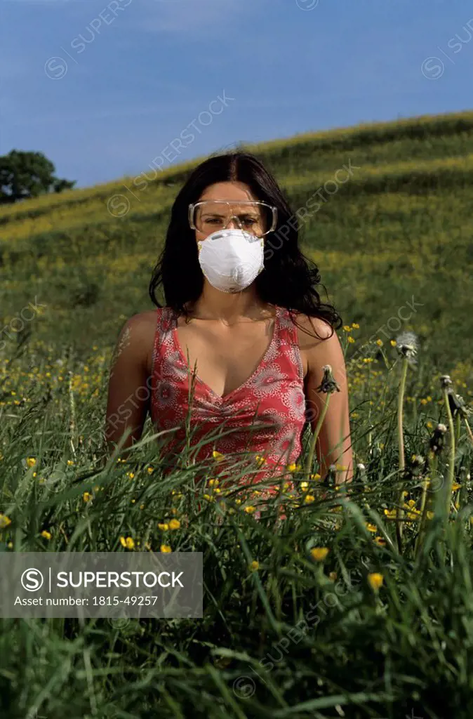 Woman wearing wearing a mask and protective goggles sitting in a meadow, avoiding pollen